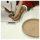 Personne utilisant une machine à coudre, fabriquant un panier MÄVINN. Jute et coton beiges ; rond, tissé à la main.
