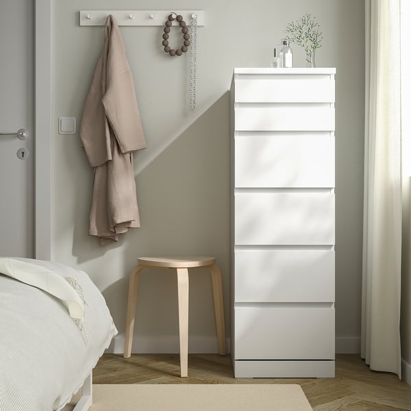 Chambre moderne avec commode MALM blanche, serviettes, collier, tabouret en bois, lit, rideau.