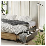 Chambre moderne avec lit en bois MANDAL, literie à pois noirs et blancs, rangement sous le lit, lampadaire et plantes.