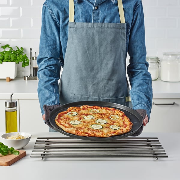 Personne tenant une pizza sur un plateau en métal, mettant en valeur une surface antiadhésive idéale pour une pizza croustillante et cuite uniformément.