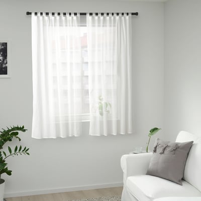 Rideaux MATILDA blancs sur tige noire, lumière douce dans une pièce minimaliste avec chaise et plantes.