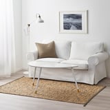 Salon minimaliste : tapis en jute MELHOLT blanc, petit canapé blanc, table basse, coussin beige, lampadaire, art encadré.