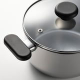 Casserole moderne en acier inoxydable avec couvercle en verre, poignées noires, prête à cuisiner.