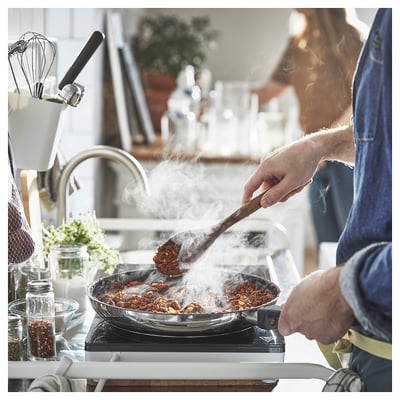 Un chef remue des aliments grésillants dans une casserole bleue sur une cuisinière dans une cuisine.