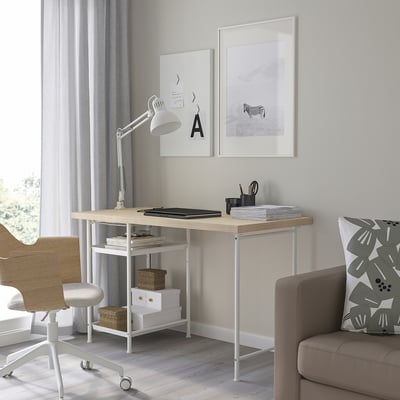 Espace de travail moderne avec bureau MITTCIRKEL, pieds réglables, lampe, œuvres d’art encadrées, chaise et ordinateur portable organisé.
