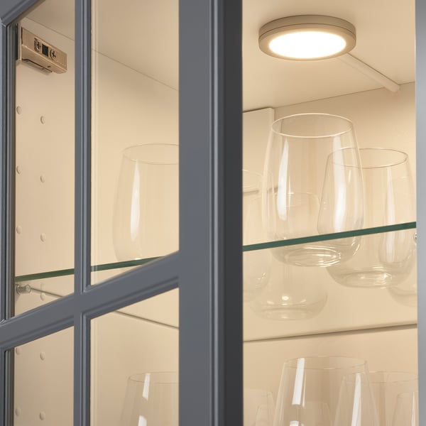 Armoire en verre avec projecteur à led intégré, éclairant des verres transparents sur les étagères.