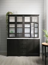 Armoire de cuisine noire moderne avec portes en verre, lumières LED, abritant divers articles de vaisselle et un comptoir en bois.