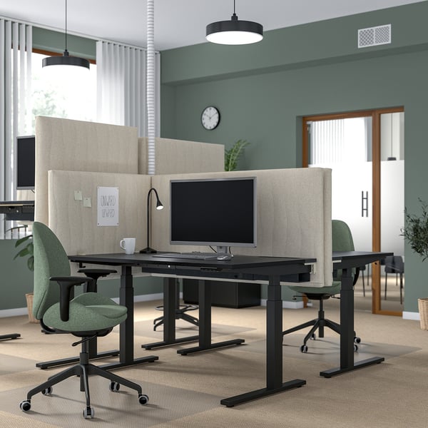 Configuration de bureau moderne avec des bureaux assis/debout MITZZON, des chaises vertes et des séparateurs beiges. Deux moniteurs, des murs verts et un bon éclairage.