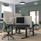 Configuration de bureau moderne avec des bureaux assis/debout MITZZON, des chaises vertes et des séparateurs beiges. Deux moniteurs, des murs verts et un bon éclairage.