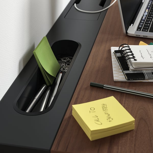 Organisateur de bureau noir avec des stylos, des trombones, des post-it et un cahier sur un bureau en bois.