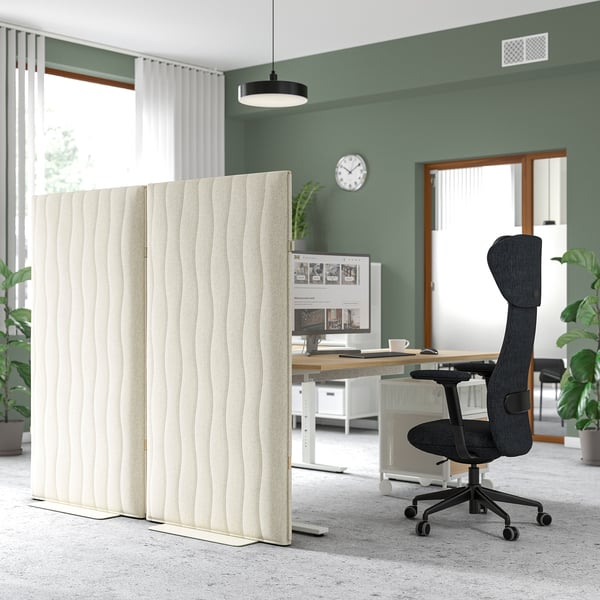 L’écran acoustique MITTZON divise le bureau. Grand, beige, bloque le son. À côté de la chaise noire, des murs verts.