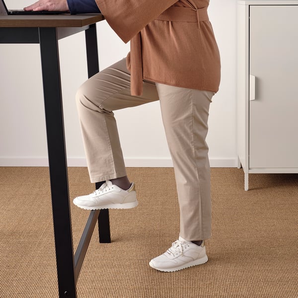 Dans une personne est debout et travaille à une table haute avec un repose-pieds, parfaite pour des réunions rapides ou des tâches en position debout.