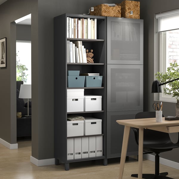 Bureau à domicile moderne avec unité de rangement, étagères et bureau MÖRTVIKEN noirs. Boîtes de rangement blanches et livres visibles. Chaise en bois et lampe sur le bureau.