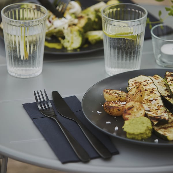 Table avec des légumes grillés, deux verres et des couverts noirs disposés dans des serviettes sombres.