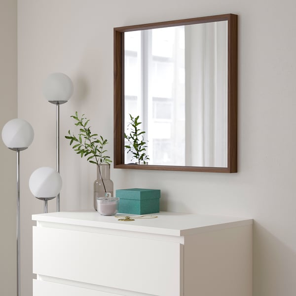 Miroir NISSEDAL sur coffre blanc, fenêtre réfléchissante, avec lampe, vase et boîte turquoise.