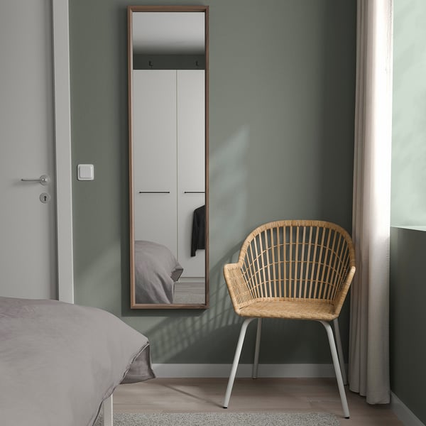Chambre minimaliste avec miroir NISSEDAL, chaise en osier et armoire. Le miroir s’appuie sur le mur vert, reflétant le lit et l’armoire.