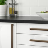 Cuisine moderne avec des armoires blanches et un comptoir sombre, avec des boutons et des poignées NYDALA dans un design élégant et minimaliste.