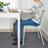 Personne assise à un bureau, utilisant un ordinateur portable et un repose-pieds pour soutenir les pieds et maintenir une bonne posture.