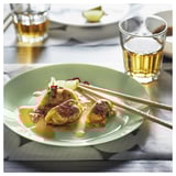 Une assiette en verre vert avec de la nourriture et des baguettes, à côté de deux verres de liquide.
