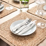 Table avec des sets de table en jute tressé, des assiettes blanches, de l’argenterie, des verres et une bougie.