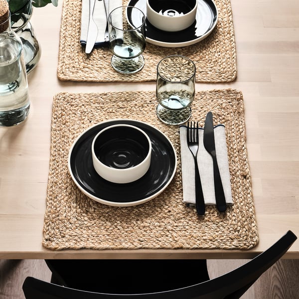 Tables dressées avec des sets de table en jute tressé, de la vaisselle noire, des verres, des couverts et des tasses.