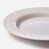 Assiette plate blanche avec rebord complexe et texturé ; semble robuste, élégant.