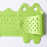 Un tapis de bain vert citron avec des ventouses, conçu pour éviter de glisser et pouvant être suspendu pour le séchage.