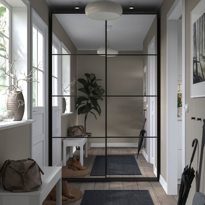 Entrée moderne avec armoire PAX grise, portes vitrées, suspension blanche, plantes et porte-manteau noir.