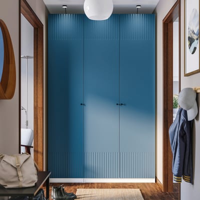 Cette image montre une armoire PAX bleue dans une pièce, plus haute qu’un porte-manteau et un porte-chapeau à proximité, avec des accents en bois et une suspension blanche au-dessus.