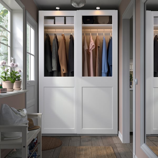 Armoire blanche ouverte, PAX, présentant des vêtements, se tient fièrement à côté de la fenêtre et du banc. Moderne et spacieux.