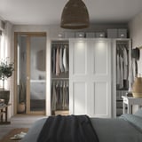 Chambre moderne avec armoire PAX blanche, vêtements ouverts, miroir, lampe, plante.
