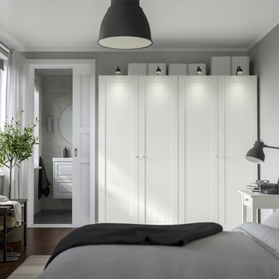 Chambre minimaliste avec armoire PAX blanche, lit gris, parquet et plante suspendue.