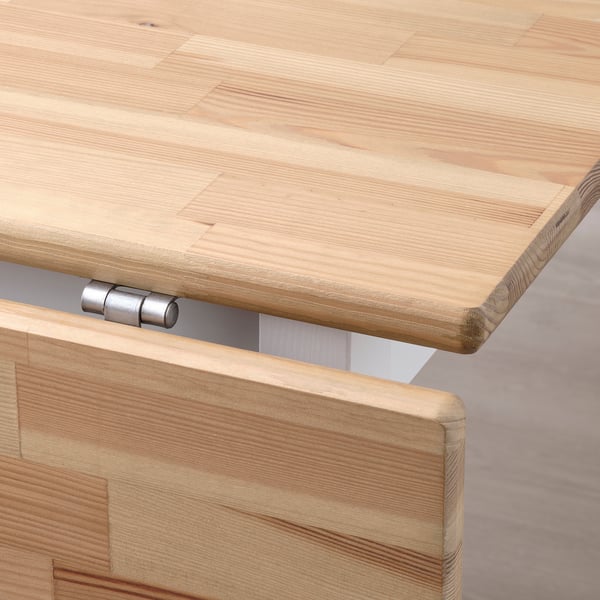 Un gros plan d’une table en bois clair avec une texture de grain visible et une charnière en métal, mettant en valeur la qualité de son savoir-faire.