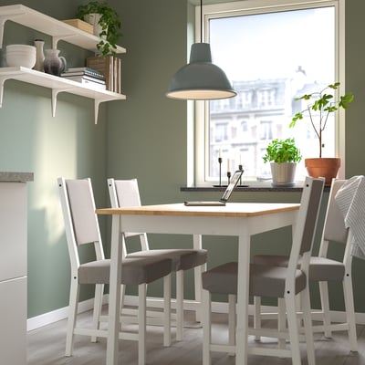 Petite salle à manger confortable avec table blanche et chaises grises, décorée de plantes vertes, sous une suspension bleue.