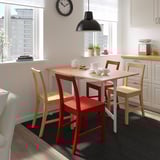 Cuisine lumineuse avec des armoires blanches, une table en bois, des chaises rouges et une horloge noire.