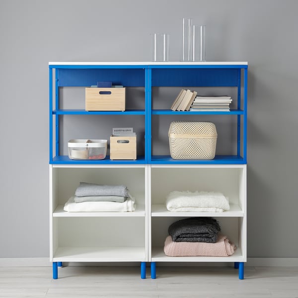 Étagère PLATSA bleue et blanche avec serviettes pliées, paniers tressés et livres empilés.