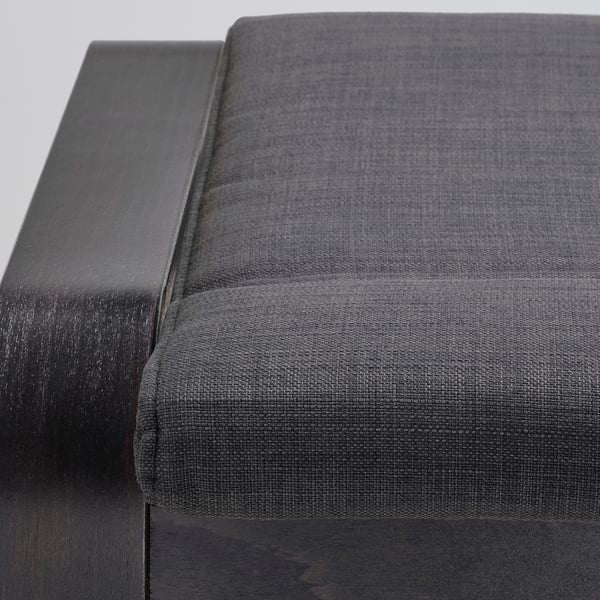 Représente un gros plan d’un repose-pieds POÄNG confortable de couleur sombre avec un cadre en bois robuste et un siège rembourré de haute qualité.
