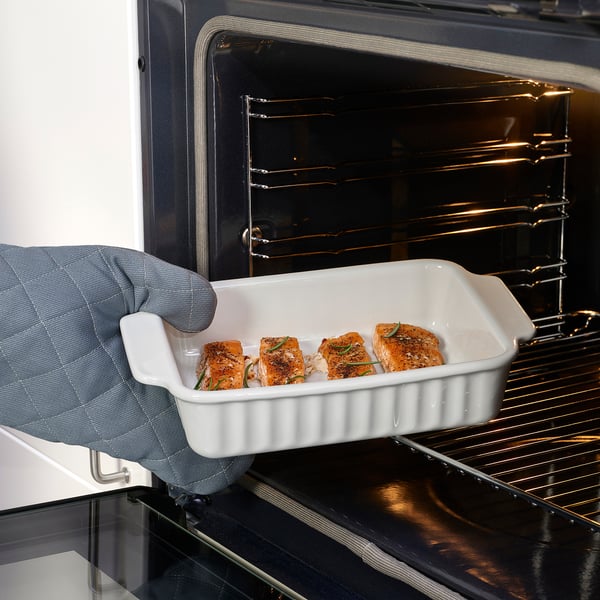 Une personne tenant un plat en céramique blanche avec du saumon rôti dans un four.