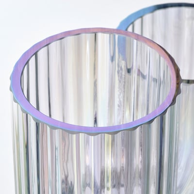 Un vase en verre RÄFFELBJÖRK, transparent avec un scintillement arc-en-ciel, doté d’un design fluide et rainuré, parfait pour les fleurs ou comme sculpture décorative.
