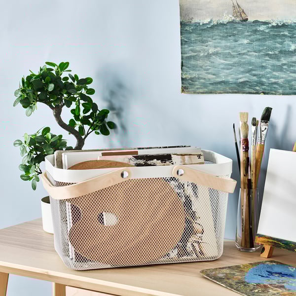 Panier RISATORP blanc avec poignées sur le bureau, contenant des papiers, des pinceaux et une plante.