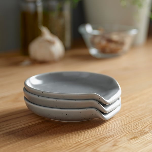 Trois repose-cuillères en grès gris empilés sur une table en bois. Empêche les ustensiles de cuisine de provoquer des déversements. Motif décoratif en pointillés. Passe au lave-vaisselle.
