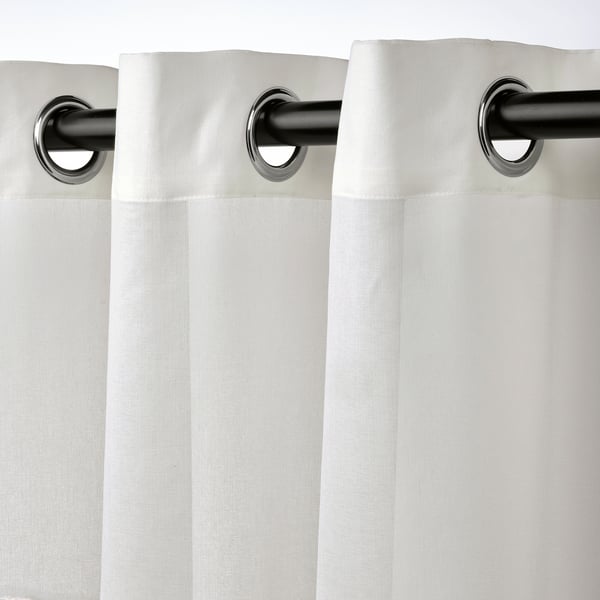 Des rideaux transparents blancs pendent d’œillets métalliques, laissant passer une lumière douce tout en ajoutant une touche moderne.
