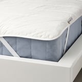 Un protège-matelas blanc avec des coins élastiques, doté d’un tissu rafraîchissant et de fibres de cire régulatrices de température, exposé sur un cadre de lit.