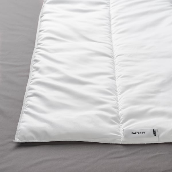 Un gros plan d’une couette blanche et lisse sur un drap sombre, mettant en valeur son tissu doux et de haute qualité et une étiquette dans le coin.