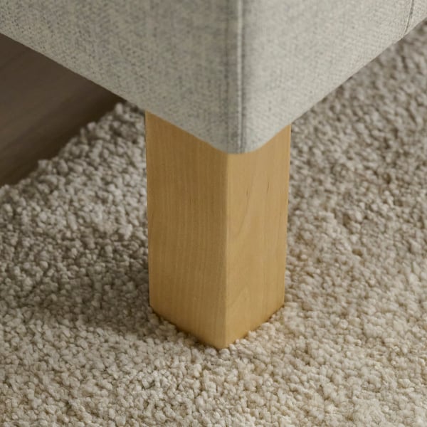 Vue rapprochée du pied en bois robuste et stylé d’un canapé sur une moquette moelleuse.