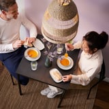 Un couple déguste une soupe à une table en sandberg noir avec une suspension en osier au-dessus de la tête.