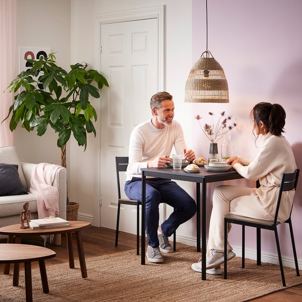 Un couple prend son petit-déjeuner à une table à manger en sandberg avec des pieds en métal et un plateau en bois dans une pièce confortable à thème rose.