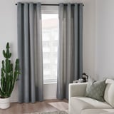Salon moderne avec rideaux gris, cactus, canapé crème, oreiller géométrique.