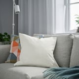 Salon moderne avec coussin blanc sur canapé gris, coussins colorés, près de la fenêtre.