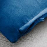 Housse de coussin bleue avec une texture lisse et veloutée et des détails de fermeture éclair, reposant sur une surface en tissu.